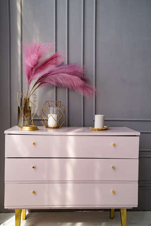 light pink dresser at the gray wall decorated with candles and colored feathers.の写真素材