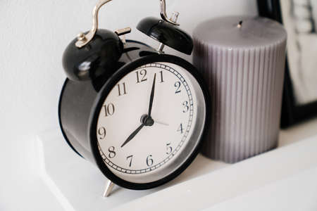 Black retro alarm clock and gray candle on white shelf.