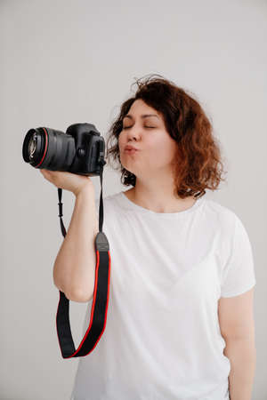 brunette woman in a T-shirt on a white background kisses camera in hand.