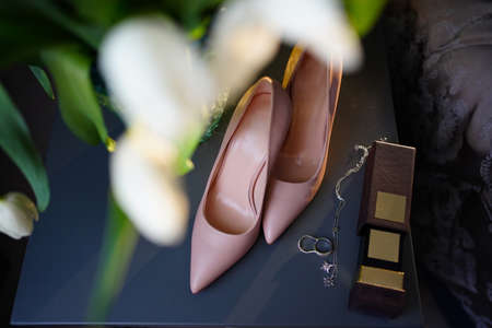 elegant high-heeled shoes, wedding rings and a chain pendant on a dark tableの写真素材