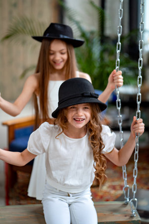 two fun beautiful girls rides in black hats on swing. original childrens roomの写真素材