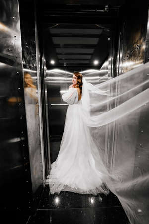 bride in a white elegant dress, with a long veil stands in a dark lift.の写真素材