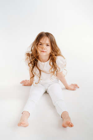 beautiful little girl with long hair in white clothes sits on the floor.の写真素材