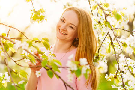 attractive woman near flowering tree in spring park. Cherry Orchard. solar glareの写真素材
