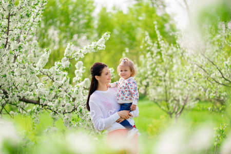 mom on a walk with a daughter in her arms in the park with a flowering trees.の写真素材