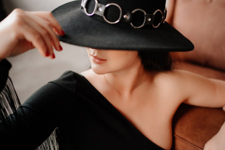 woman with dark hair in black bodysuit and hat by leather chairの写真素材