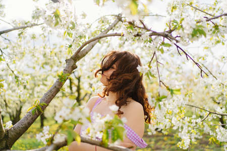 attractive woman with blowing hair near flowering tree in spring park.