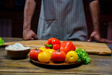 a wooden bowl of flour and vegetables on the kitchen table. man in an apron.の写真素材