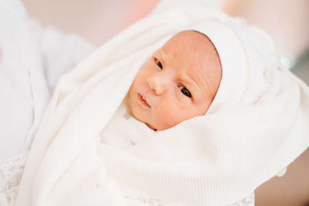 Newborn in white clothes on hands of parent. attire for discharge from hospitalの写真素材