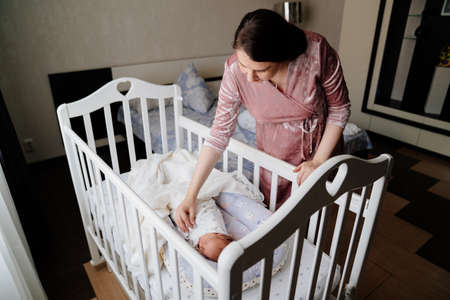 Mom straighten the blanket at the sleeping in the crib of the newborn.の写真素材