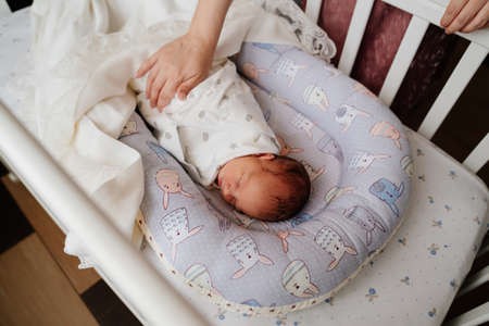 Moms hands straighten the blanket at the sleeping in the crib of the newborn.