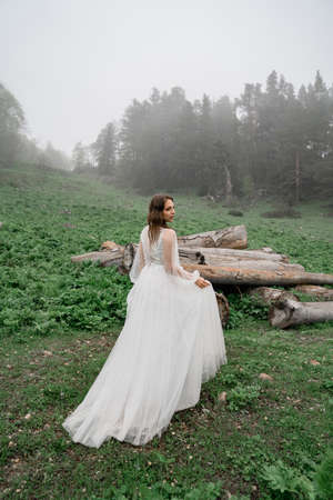 The bride in a white wedding dress stands in a field by the logs.の写真素材