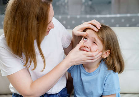 little girl complains to her mother about the pain in her eyes.の写真素材