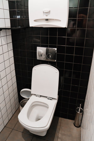 toilet in a small toilet room with black and white ceramic tiles on the walls.の写真素材
