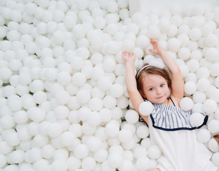 cheerful little girl in a dry pool with white balls. playground.の写真素材