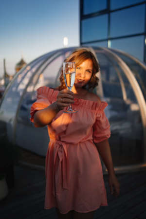 at sunset. beautiful woman in a pink dress on the roof with a glass of champagne