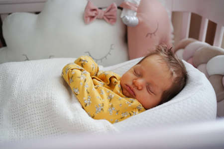 newborn in a yellow jumpsuit lies in a retainer of the child in a crib