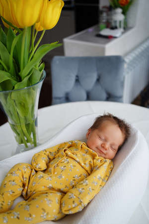 newborn baby in a yellow jumpsuit lies in a retainer for the safety of the child
