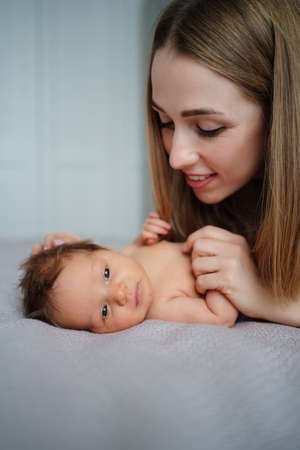 mom gently looks at the baby on bed. maternal love and care. care for newbornsの写真素材