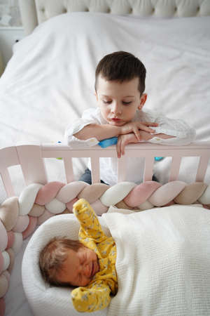 the older brother watches the crying younger sister in the crib.の写真素材