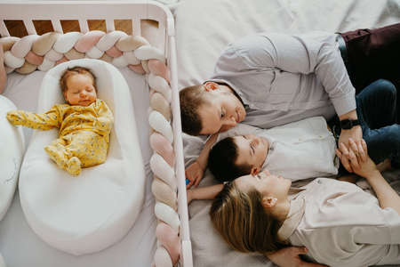 a family with an eldest son lies at the crib with a newborn baby.の写真素材