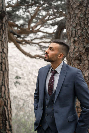 attractive man with beard in business suit stands at trunks of trees in forest.の写真素材