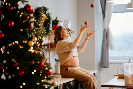 a beautiful pregnant woman sits on the table and juggling in New Years kitchen.の写真素材