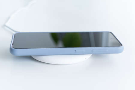 the smartphone is placed on a white round wireless charger.の写真素材