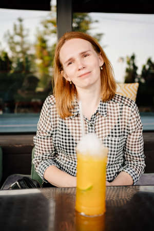 young woman drinks through cocktail tube tropical cocktail. family cafe, summer verandaの写真素材