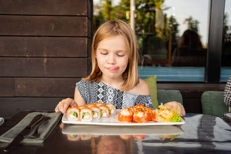 little girl in cafe restaurant, country house smiles and licks looks sushi rollsの写真素材