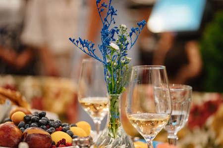 a glass of white wine and a bouquet of blue flowers on the served table.