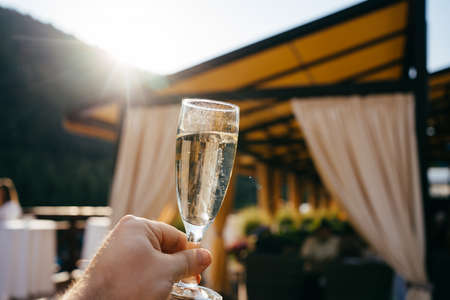 hand with glass of champagne against the background of the canopy of the terraceの写真素材