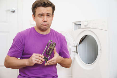 repairman of washing machine holds old tubular electric heaterの写真素材