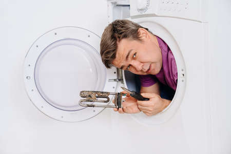 repairman of washing machine holds tubular electric heater and screwdriverの写真素材