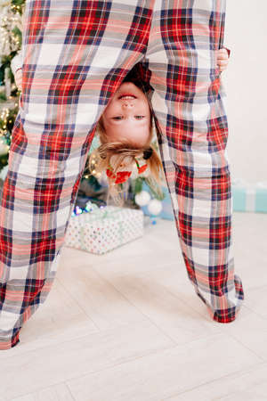 dad and little daughter in red plaid pajamas playing at the Christmas treeの写真素材