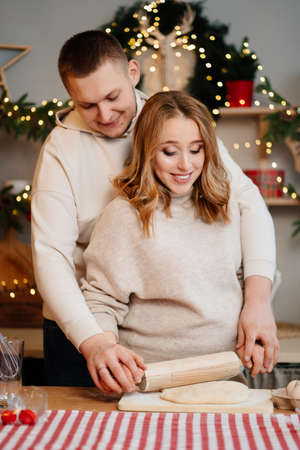pregnant woman with husband in New Year kitchen roll out dough with rolling pinの写真素材
