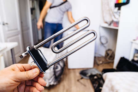 repair of washing machine. new tubular electric heater in hands of a repairmanの写真素材