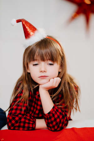 kid girl in a red plaid dress and cap make a wish in the New Years interior.の写真素材