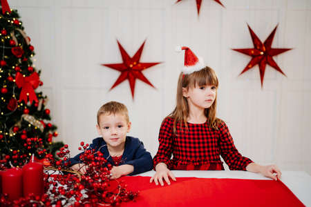 little boy and girl at the festive Christmas table with a red tablecloth.の写真素材