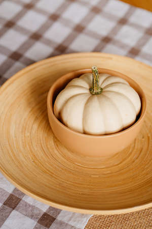 a small decorative white pumpkin in a clay bowl on a wooden platter.の写真素材