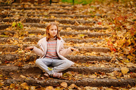 a cute little girl sitting on a staircase with fallen foliage in an autumn park.の写真素材