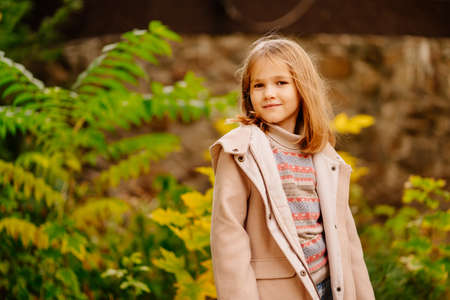 a cute little girl in a coat and jeans in an autumn park with yellowing foliage.の写真素材
