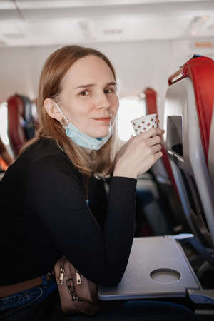 a woman in a protective mask drinks a drink from a paper cup on board the plane.の写真素材