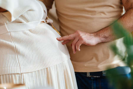 a mans hand touches the abdomen of a pregnant woman with his fingers.