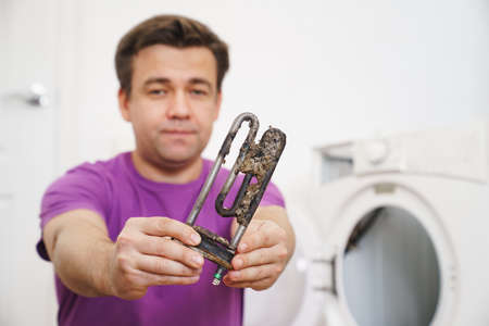 repairman of washing machine holds old tubular electric heaterの写真素材