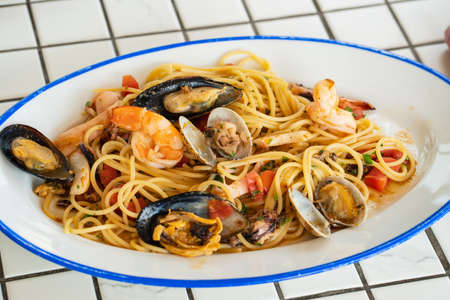 spaghetti with seafood in an oval plate on a table with a plaid tablecloth.の写真素材