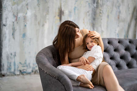 Mom on the couch cuddles with her daughter. happy family.の写真素材