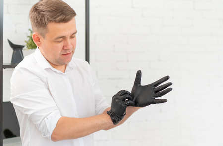 a man in a white shirt wears black rubber gloves against a white wall.の写真素材
