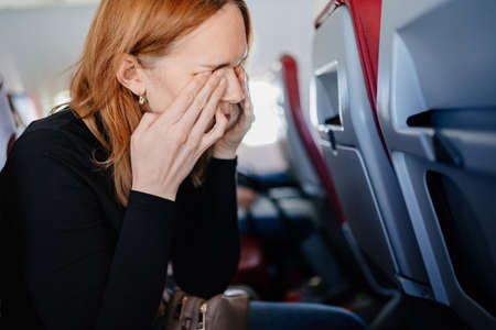 a sleepy woman rubs eyes with hands in an airplane seat. long flights.の写真素材