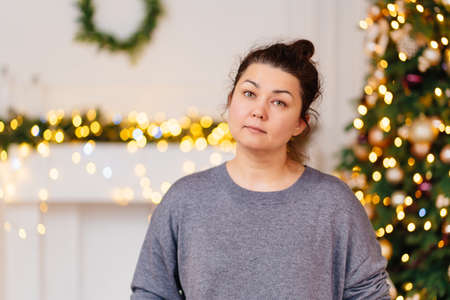 woman with dark bunded hair, no makeup in room with Christmas tree and garland.